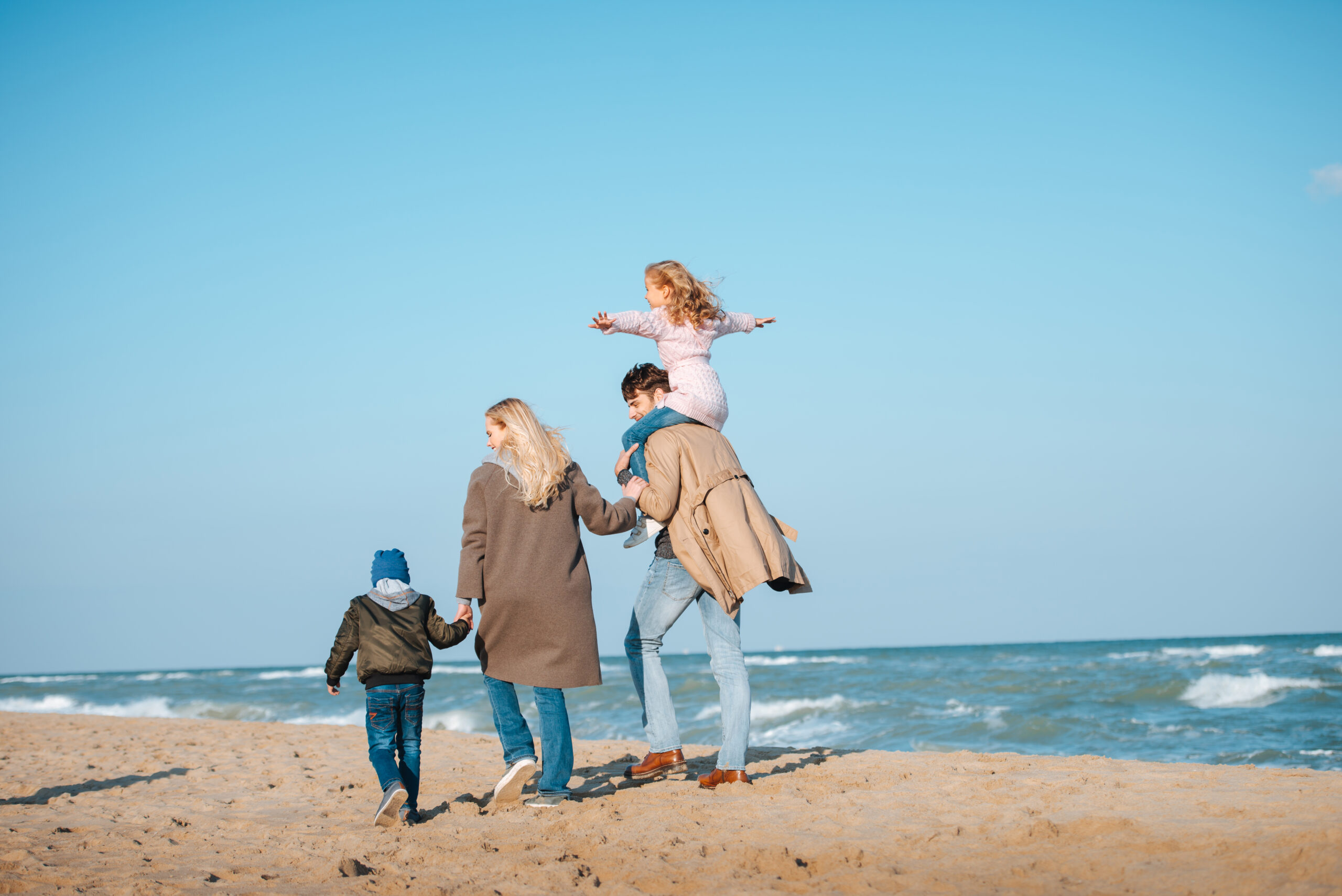 parents walking with kids on seashore in autumn